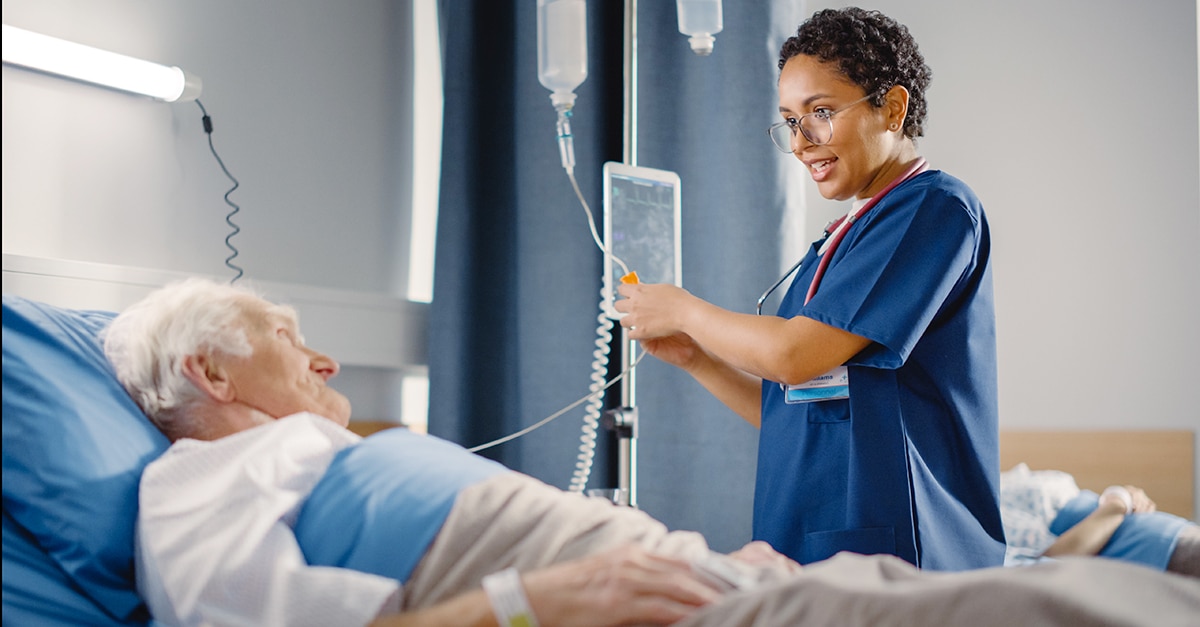 Friendly Female Head Nurse Making Rounds does Checkup on Elderly Patient Resting in Bed.